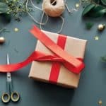 a box being wrapped in brown paper and a red ribbon as a Christmas gift.