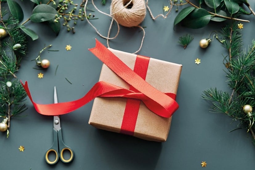 a box being wrapped in brown paper and a red ribbon as a Christmas gift.